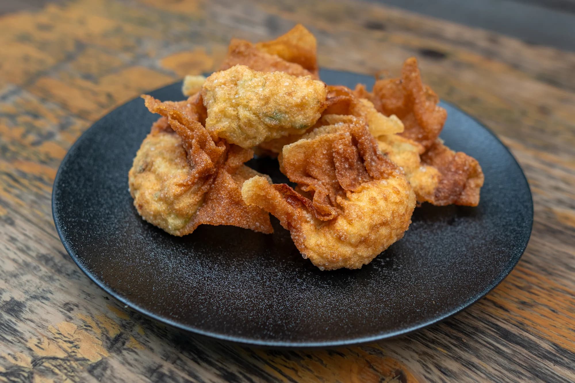 Golden fried wontons on a textured black plate at Viet Nom Nom, New Plymouth