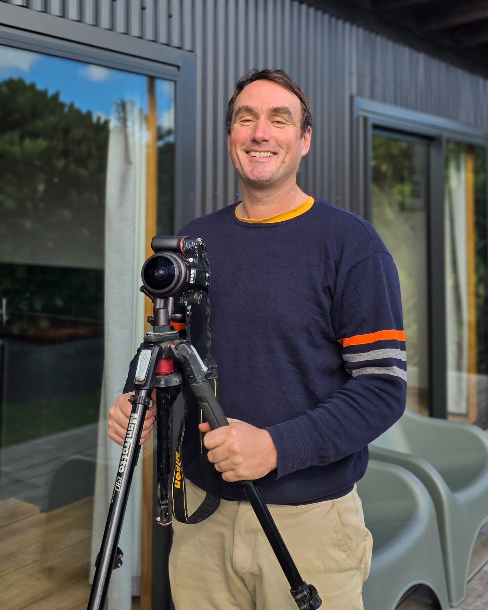 Tamron Galbraith holding a camera and tripod outside a local business
